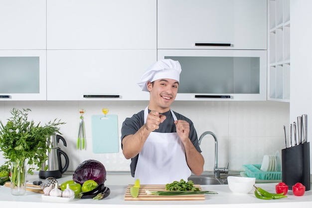 Vista frontal feliz jovem chef de uniforme apontando para a câmera