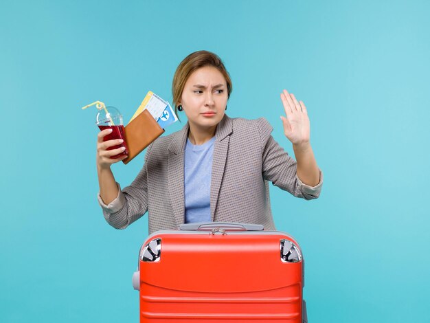 Vista frontal feminina em férias segurando suco com ingressos em fundo azul claro viagem férias viagem viagem hidroavião