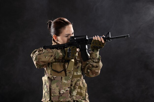 Vista frontal feminina soldado de uniforme com rifle na parede preta