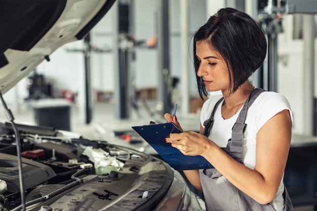 Vista frontal feminino mecânico inspecionando carro