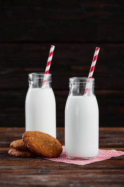 Vista frontal garrafas de leite com canudos e biscoitos