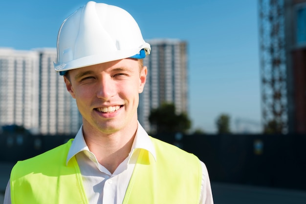 Vista frontal homem sorridente com capacete de segurança e colete