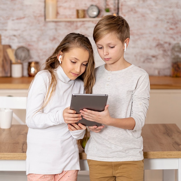 Vista frontal irmãos pouco olhando juntos em um tablet