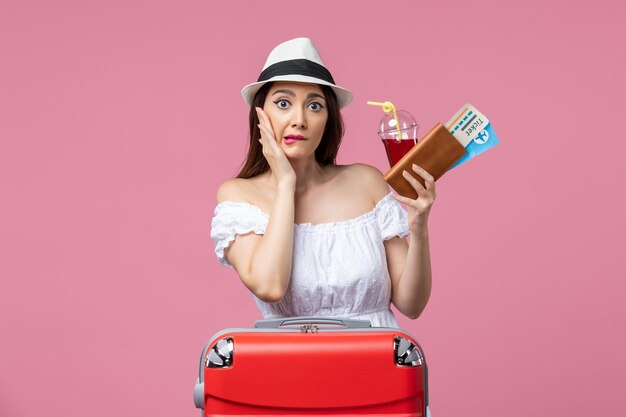 Vista frontal jovem bebendo suco segurando ingressos de férias na parede rosa verão viagem mulher viagem resto