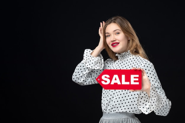 Vista frontal jovem bonita mulher segurando venda escrita em uma parede preta cor vermelha compras foto emoção moda mulher