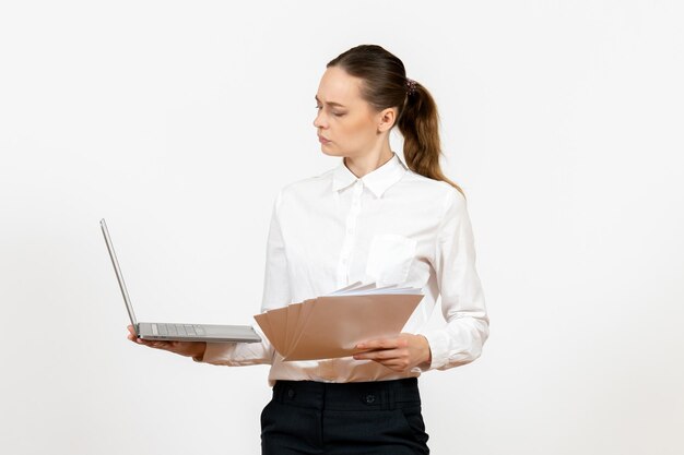 Vista frontal jovem com blusa branca segurando laptop e documentos na mesa branca modelo de sentimento de emoção de escritório de trabalho feminino