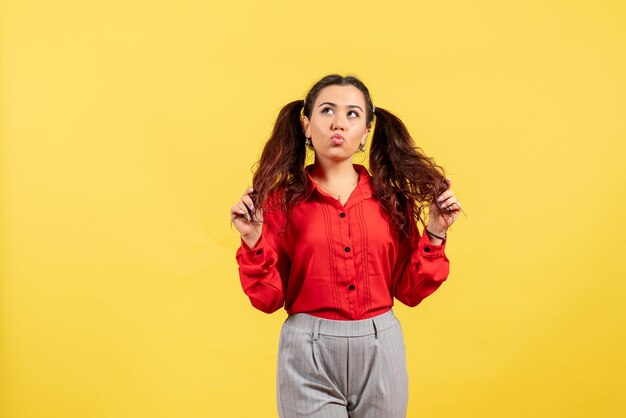 Vista frontal jovem com blusa vermelha com cabelo bonito, posando em fundo amarelo.