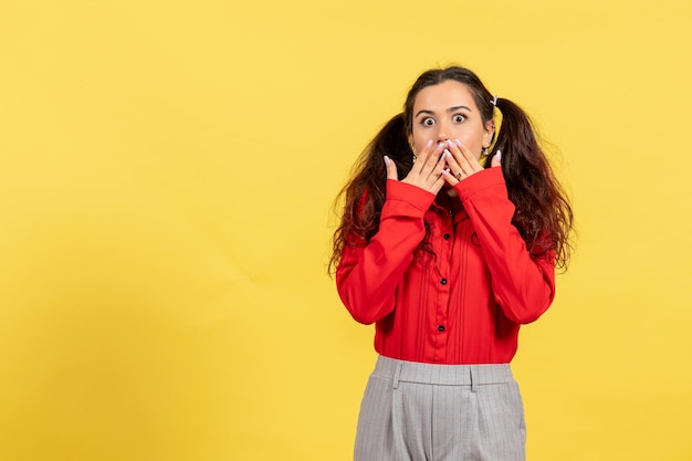 Vista frontal jovem com blusa vermelha com cabelo fofo e rosto surpreso com fundo amarelo inocência criança menina juventude cor criança