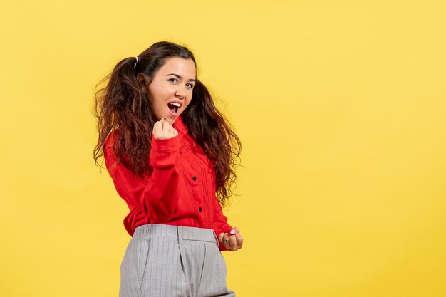 Vista frontal jovem com blusa vermelha com cabelo fofo regozijando-se com fundo amarelo criança cor criança menina juventude inocência