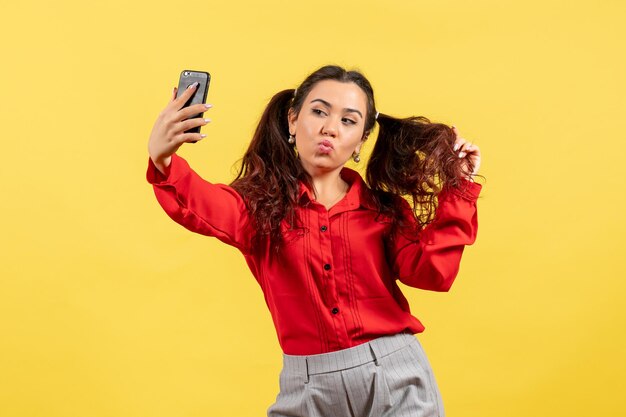 Vista frontal jovem com blusa vermelha com cabelo fofo tomando selfie sobre fundo amarelo.