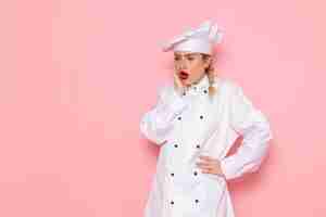 Foto grátis vista frontal jovem cozinheira em terno branco de cozinheiro posando com expressão de surpresa na foto de trabalho de cozinha de cozinha de espaço rosa