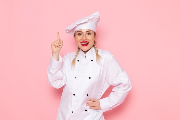 Foto grátis vista frontal jovem cozinheira em terno branco posando sorrindo no espaço rosa cozinhar cozinha trabalho trabalho foto