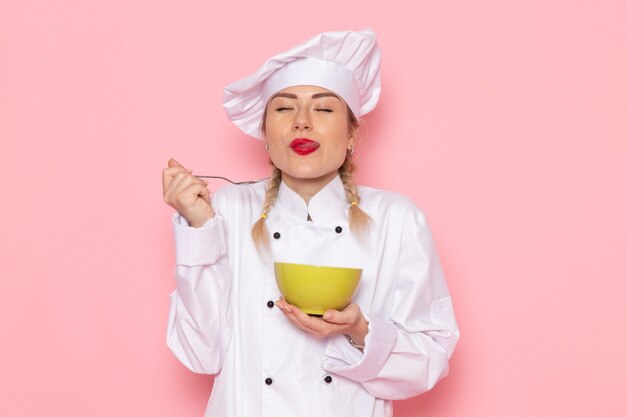 Vista frontal jovem cozinheira em traje de cozinheira branco segurando um prato verde e provando-o no cozinheiro espacial rosa