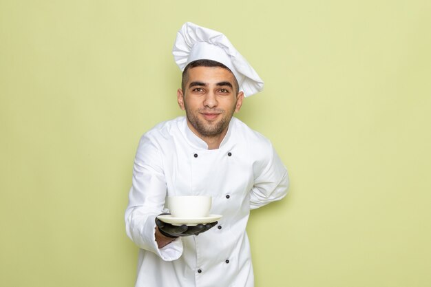 Vista frontal jovem cozinheiro masculino em terno branco de cozinheiro usando luvas escuras e segurando o café para entrega