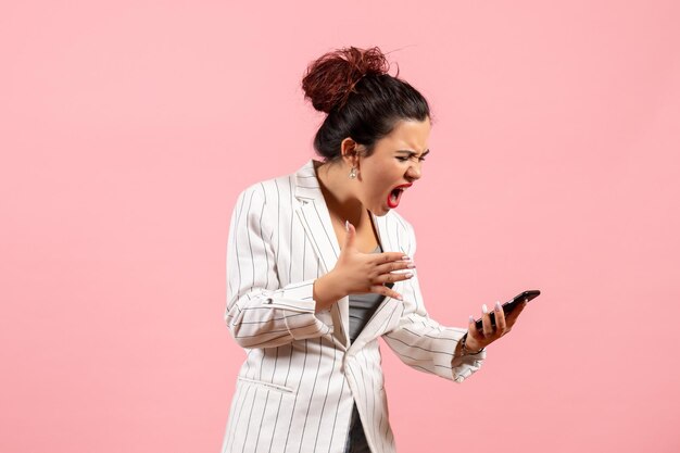 Vista frontal jovem de jaqueta branca segurando o telefone e gritando com ele no fundo rosa moda mulher emoção sentimento senhora cor