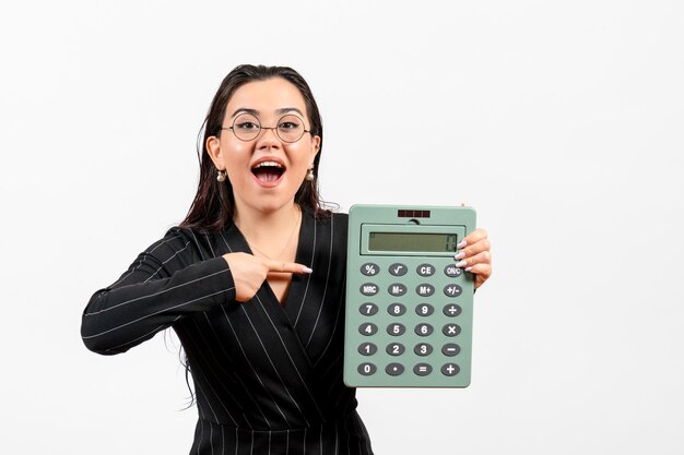 Vista frontal jovem de terno escuro segurando calculadora no fundo branco trabalho mulher moda negócios beleza escritório