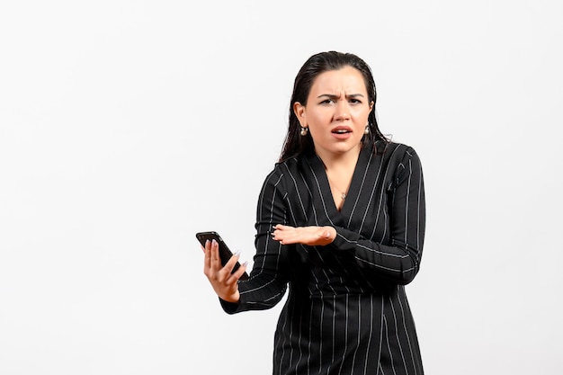 Vista frontal jovem de terno escuro segurando o telefone no fundo branco Mulher senhora moda escritório trabalhador trabalho beleza