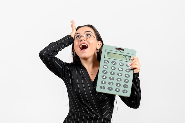 Foto grátis vista frontal jovem de terno escuro segurando uma calculadora no fundo branco-claro trabalho mulher escritório moda negócios beleza