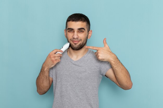 Vista frontal jovem do sexo masculino com camiseta cinza barbeando a barba na espuma azul gelo para cabelo masculino para barba de barbear