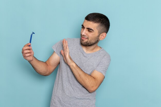 Vista frontal jovem do sexo masculino com camiseta cinza segurando navalha na barba de barbear azul, cabelo masculino, cor de espuma