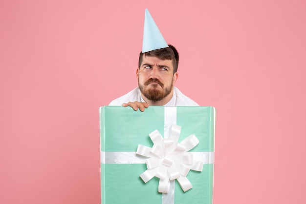 Vista frontal jovem do sexo masculino em pé dentro da caixa de presente na mesa rosa foto de natal festa do pijama
