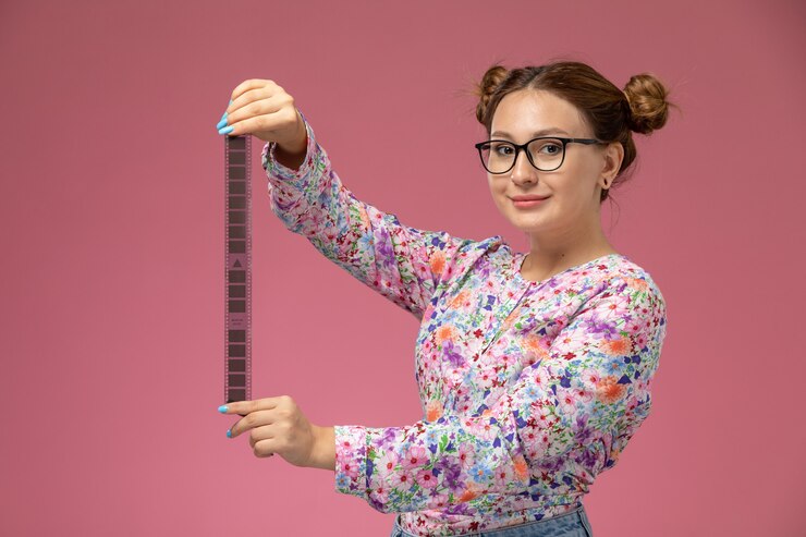 Foto grátis vista frontal, jovem e linda mulher em uma camisa com design flor e calça jeans segurando uma fita de cinema antiga no fundo rosa