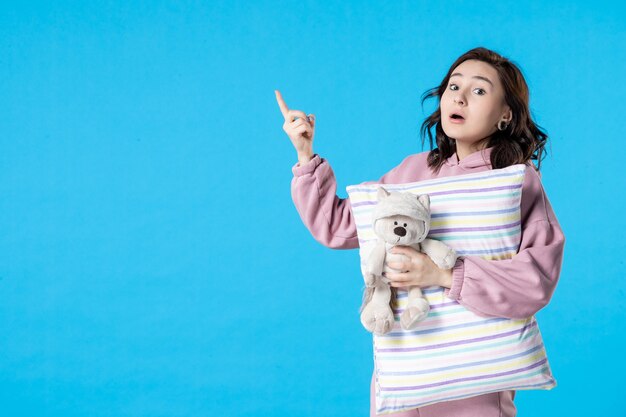 Vista frontal jovem feminina de pijama rosa com ursinho de brinquedo e travesseiro na cama de mulher azul noite descanso insônia sonho festa sono