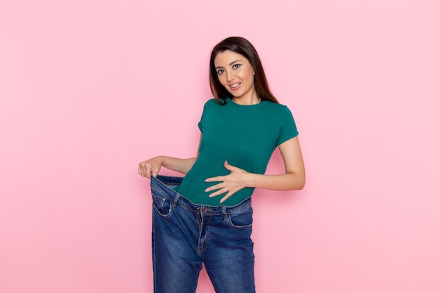 Foto grátis vista frontal jovem feminino em uma camiseta verde, verificando sua cintura na parede rosa claro cintura esporte exercícios exercícios beleza magro atleta feminino