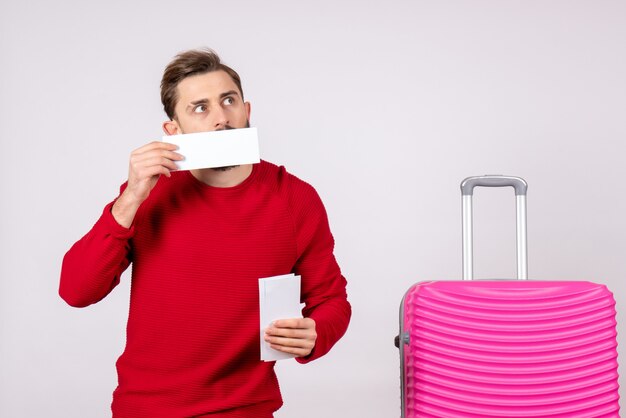 Vista frontal jovem homem com bolsa rosa e segurando bilhetes na parede branca viagem voo férias viagem verão turista