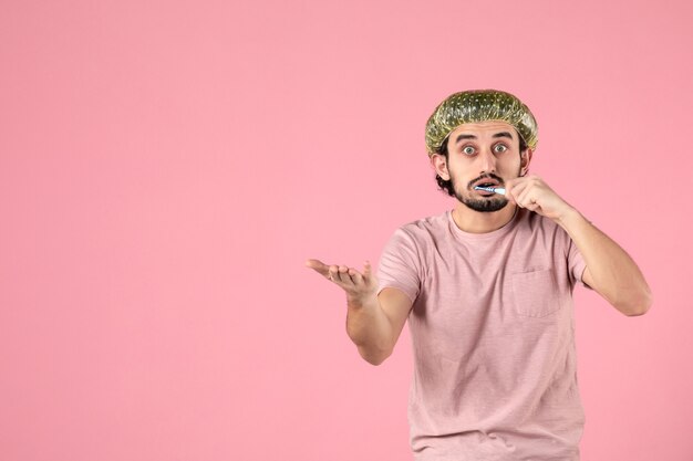 vista frontal jovem homem limpando os dentes em fundo rosa