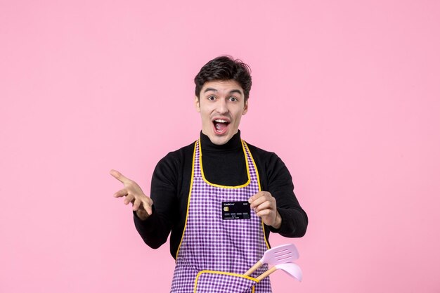 Vista frontal jovem homem na capa segurando cartão de banco preto no fundo rosa profissão de trabalho cozinhar chefe uniforme trabalhador dinheiro cozinha horizontal