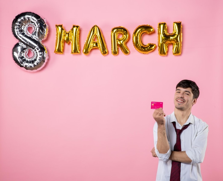 Foto grátis vista frontal jovem homem segurando cartão de banco rosa com decoração de março em fundo rosa igualdade feminina cor dinheiro feriado homem presente compras