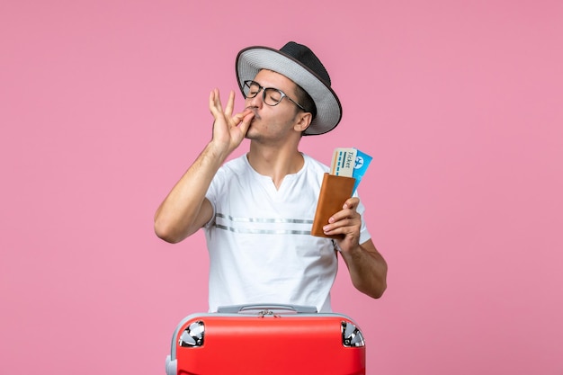 Vista frontal jovem homem usando chapéu e segurando passagens de avião na parede rosa viagem viagem avião foto colorida férias