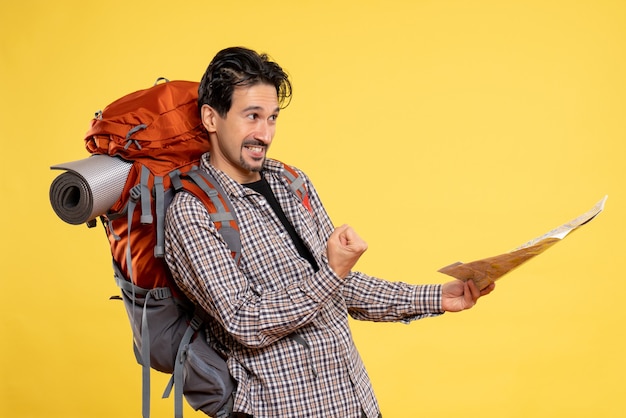 Vista frontal jovem indo em caminhada com mochila segurando mapa em cor de floresta de campus de viagem de companhia aérea de fundo amarelo