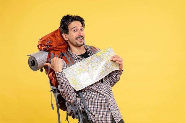 Vista frontal jovem indo em caminhadas com uma mochila segurando um mapa em fundo amarelo