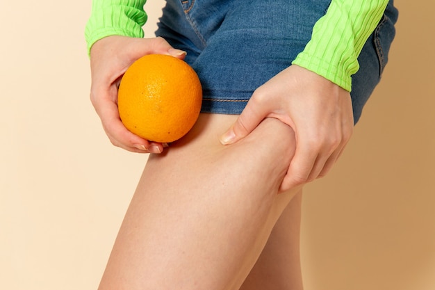 Vista frontal jovem linda mulher com camisa verde segurando uma laranja na parede creme fruta modelo mulher suave