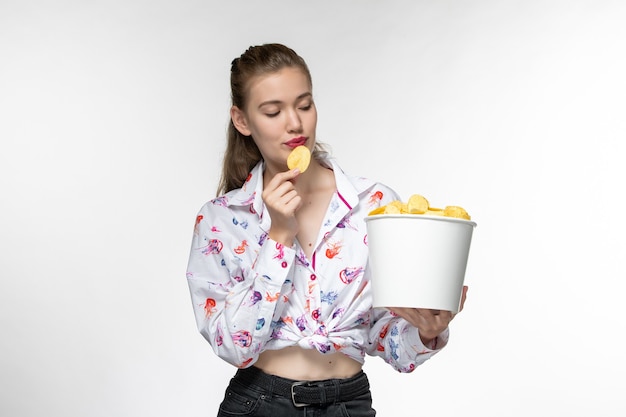 Foto grátis vista frontal jovem linda mulher comendo batata cips e assistindo filme na superfície branca