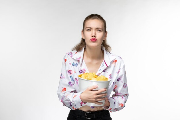 Vista frontal jovem linda mulher segurando a cesta com batata cips na superfície branca