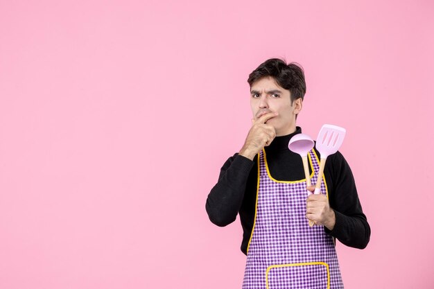Vista frontal jovem macho na capa segurando colheres no fundo rosa trabalho massa profissão cozinha uniforme horizontal cozinheiro chefe cor principal