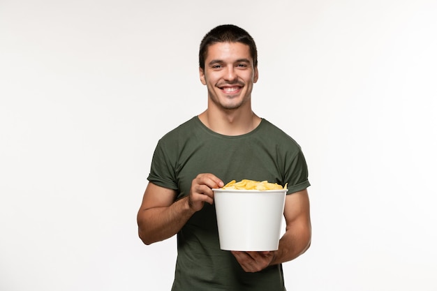 Foto grátis vista frontal jovem masculino com camiseta verde com batata cips assistindo filme e sorrindo na parede branca filme pessoa masculino filme solitário cinema