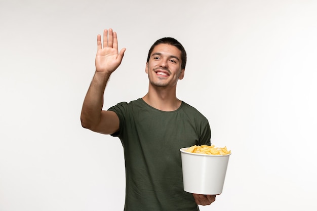 Vista frontal jovem masculino em uma camiseta verde com batata cips e cumprimentando alguém na parede branca filme pessoa masculino filme solitário cinema