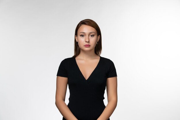 Vista frontal, jovem mulher atraente de camisa preta, parada na superfície branca