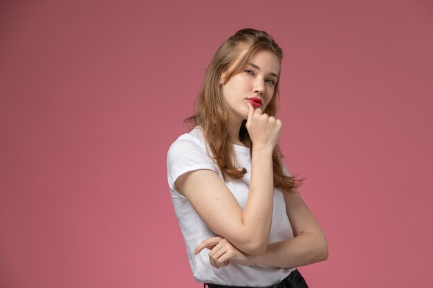 Vista frontal jovem mulher atraente em camiseta branca, posando com a expressão do pensamento na parede rosa modelo feminino pose foto colorida