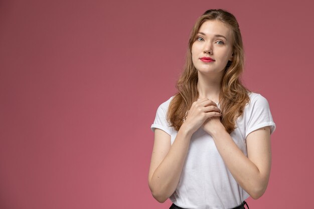 Vista frontal jovem mulher atraente em camiseta branca posando com uma expressão fofa na parede rosa modelo feminino pose foto colorida feminino jovem