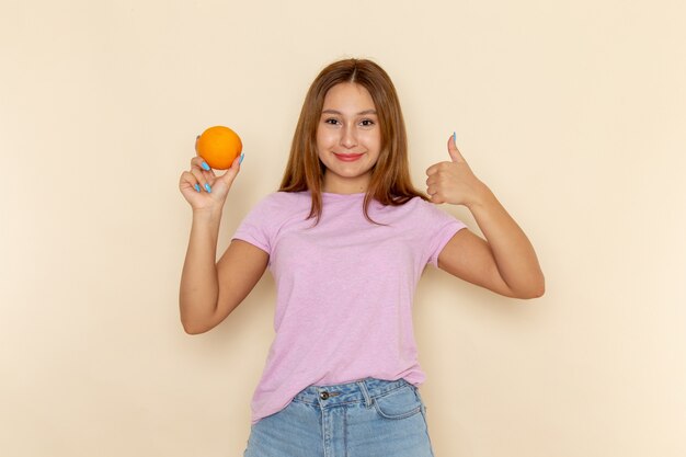 Vista frontal jovem mulher atraente em camiseta rosa e jeans azul segurando laranja e mostrando uma placa incrível