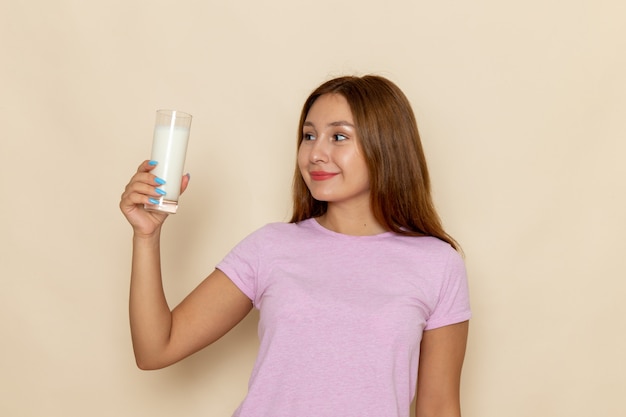 Vista frontal, jovem mulher atraente em camiseta rosa e jeans azul segurando um copo de leite