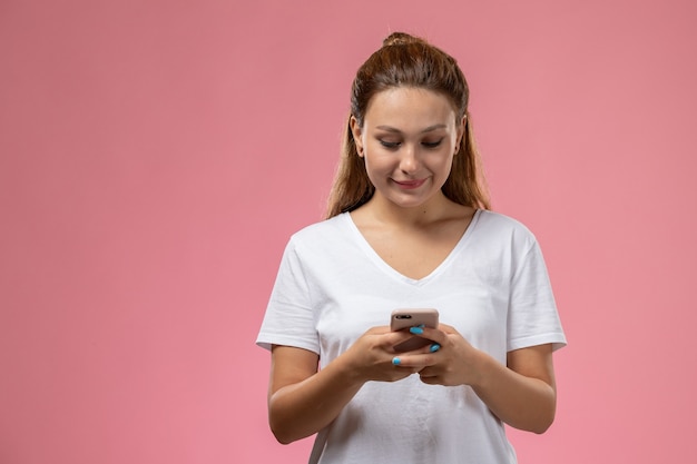 Foto grátis vista frontal jovem mulher atraente em smi camiseta branca e usando um telefone no fundo rosa