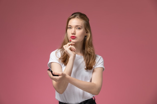 Vista frontal jovem mulher atraente em uma camiseta branca fazendo sua maquiagem na parede rosa cor do modelo feminino jovem
