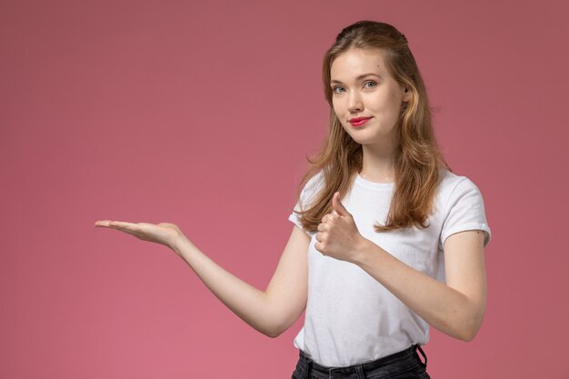 Vista frontal jovem mulher atraente sorrindo e mostrando a palma da mão na parede rosa escuro cor do modelo feminino jovem
