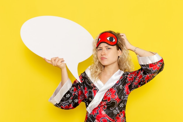 Vista frontal jovem mulher com roupão segurando uma enorme placa branca na parede amarela cama noturna modelo menina cor